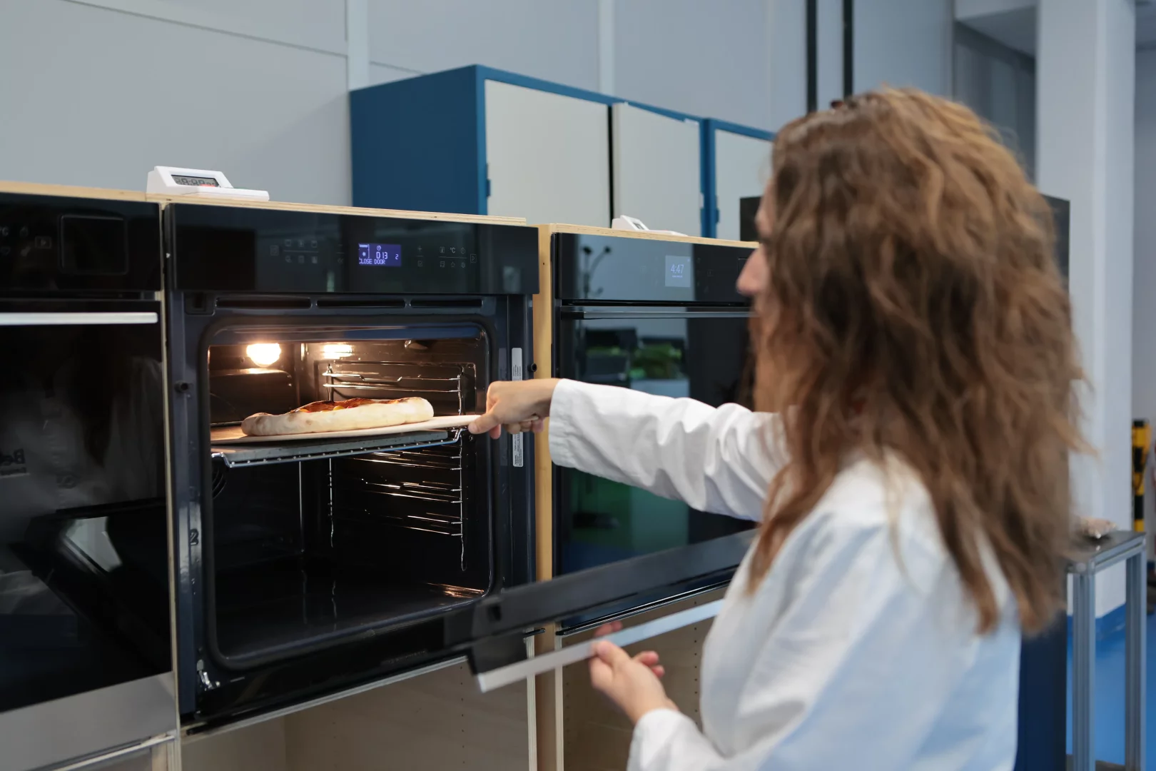 Modern, aydınlık bir Food Tech Lab mutfak ortamında, ankastre fırın, şık bir indüksiyonlu ocak ve stand mikser gibi çağdaş beyaz eşyalar, İtalya'daki tesislerde geliştirilen yapay zekâlı mutfak teknolojileri ve sessiz lüks tasarım felsefesini yansıtan detaylarla sunuluyor.