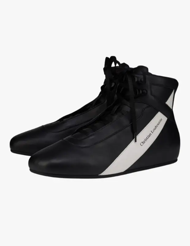 Beyaz bir zeminde duran, Christian Louboutin marka, yanlarında beyaz çapraz bir şerit ve üzerinde Christian Louboutin yazısı olan, bağcıklı ve bilekli iki adet siyah erkek spor ayakkabısı, markanın zarif Sonbahar Kış koleksiyonunu temsil ediyor.
