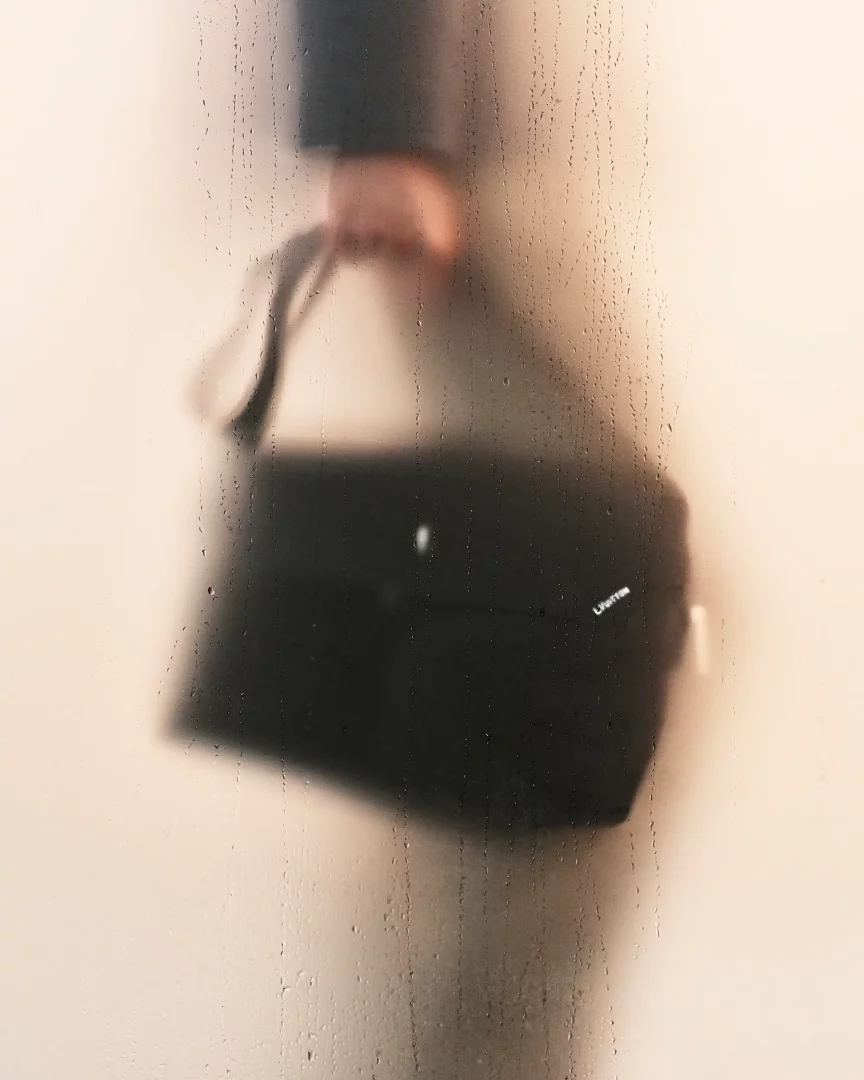 Bu bulanık görüntüde, yağmur damlalarıyla kaplı bir camın ardından bir elin tuttuğu siyah bir omuz çantası belirginleşiyor; bu, Louis Vuitton İlkbahar/Yaz 2027 ön koleksiyonundan bir parçayı gizemli bir şekilde sunuyor.