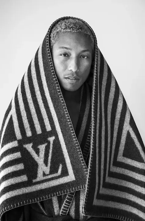 Siyah beyaz bir fotoğrafta, başını ve vücudunu Louis Vuitton logolu, çizgili, kenarları belirgin dikişli bir battaniyeye sarmış, kameraya doğru bakan Pharrell Williams'ın düşünceli portresi, lüks marka iş birliğini vurguluyor.