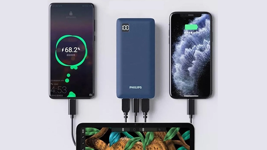 Ortada duran, ekranında yüzde 100 şarj seviyesini gösteren mavi Philips power bank, üç siyah kabloyla eş zamanlı olarak iki akıllı telefonu (biri yüzde 68.2, diğeri yüzde 100 şarjda) ve altta kısmen görünen bir tableti şarj ediyor; 22.5W PD hızlı şarj yeteneğini vurgulayan bu görüntü, çoklu cihaz şarj kolaylığını sergiliyor.