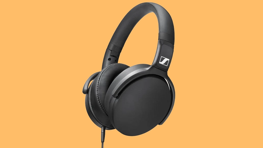 Canlı turuncu bir arka plan önünde, sağa doğru hafifçe eğimli duran, dış yüzeyinde belirgin beyaz Sennheiser logosu bulunan, kablolu ve mat siyah renkli, kulağı tamamen saran bir Sennheiser HD 400S kulaklık modeli görülüyor.