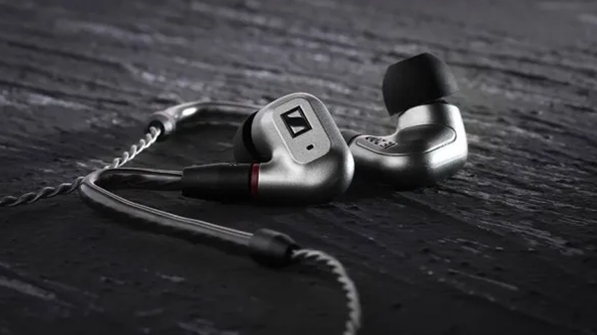 Koyu, dokulu bir zeminde konumlandırılmış, gümüş rengi metalik kasalı, siyah uçlu ve örgülü kablolu Sennheiser IE 200 üst düzey kulak içi kulaklıklar, net detaylarıyla öne çıkıyor.