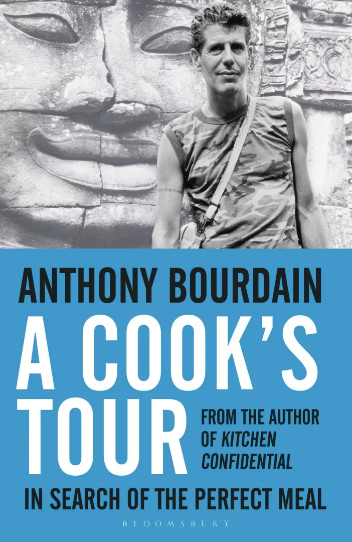 Anthony Bourdain'in 'A Cook's Tour' adlı kitabının kapağı, kamuflaj desenli kolsuz tişörtüyle, arkasında büyük bir taş oyma yüzün bulunduğu siyah beyaz bir fotoğrafını ve kitabın adını parlak mavi zemin üzerinde gösteriyor.