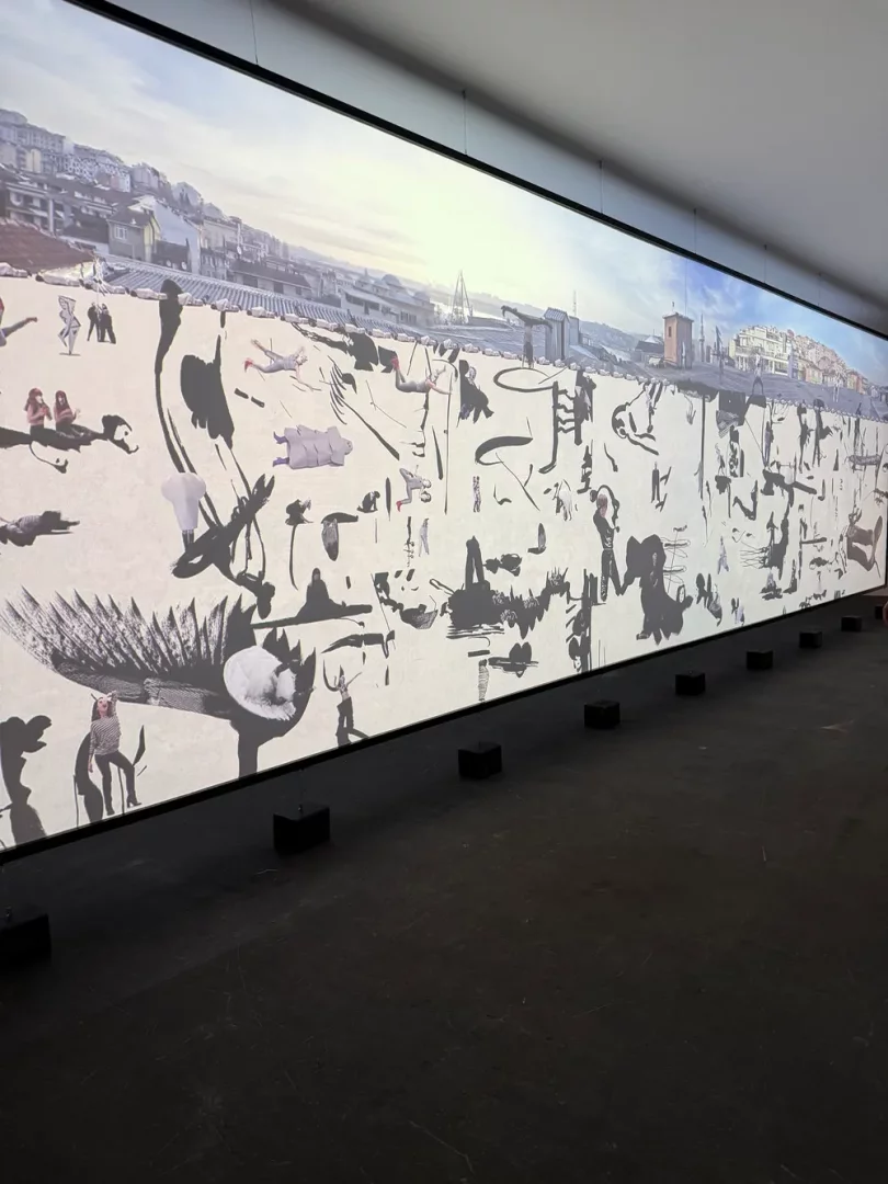 Geniş bir ekrana yansıtılmış Art Basel koleksiyonundan bir sanat eseri; üstte gri tonlarda şehir silüetleri, altta ise beyaz zemin üzerinde soyut siyah fırça darbeleri, kuş ve insan figürleri ile birkaç renkli insan silüetinin birleştiği gerçeküstü ve dinamik bir kompozisyon sunuyor.