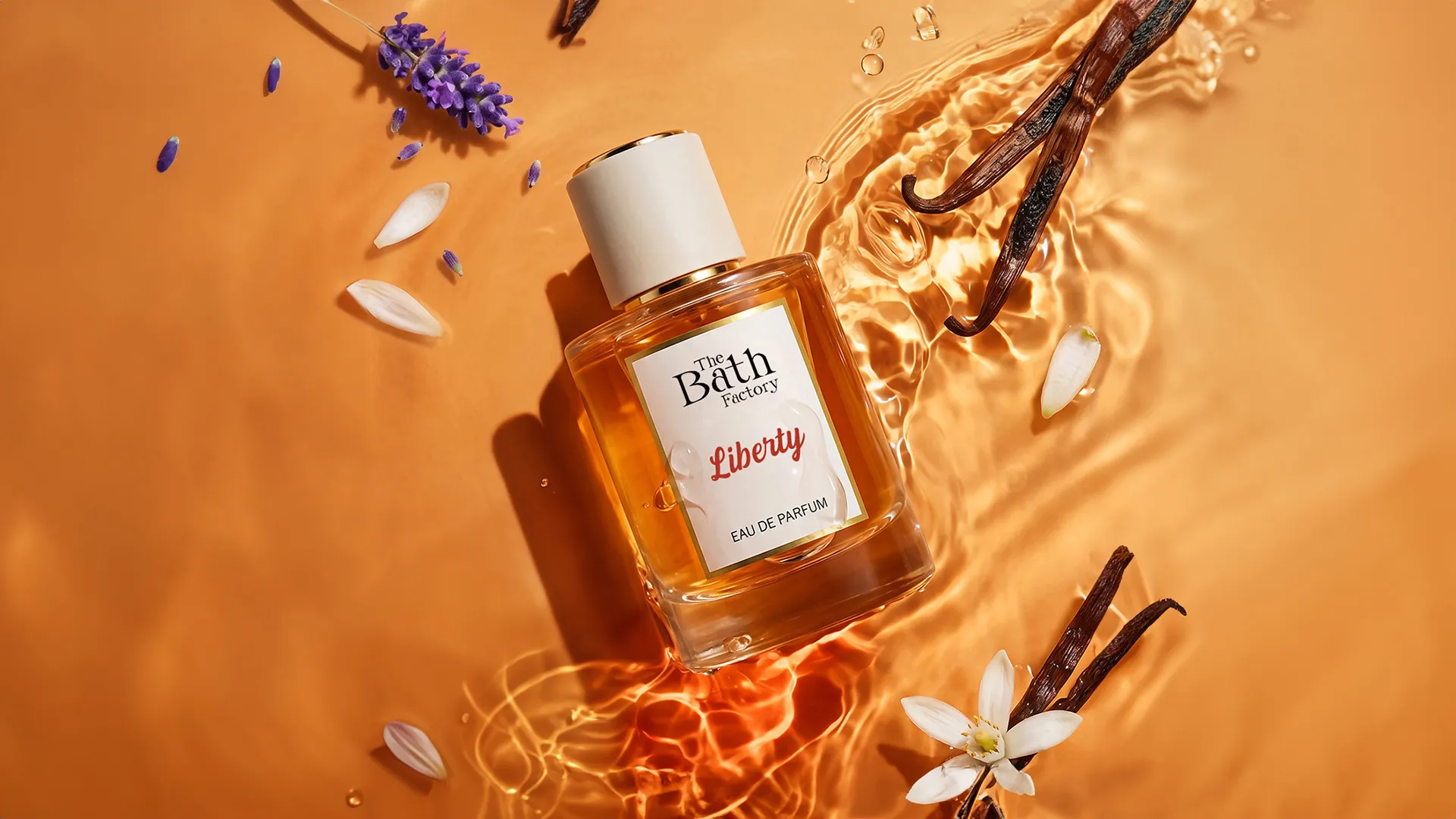 Turuncu bir arka plan üzerinde, su damlacıkları ve hafif dalgalanmalarla çevrili, The Bath Factory Liberty Eau de Parfum yazan kehribar rengi bir parfüm şişesi, lavanta çiçekleri, vanilya çubukları ve beyaz bir çiçeğin eşlik ettiği bu düzenlemeyle markanın haziran ayındaki yeni gelişmelerini temsil ediyor.