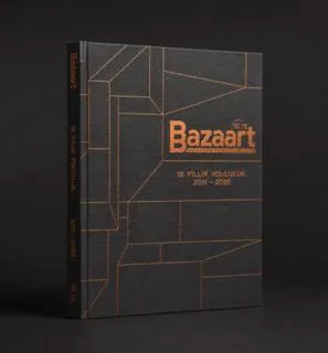 Koyu gri zemin üzerine metalik bakır rengi Bazaart logosu ve 2011-2026 15 Yıllık Yolculuk yazısı ile geometrik çizgilerin yer aldığı, Bazaart'ın önemli bir dönüm noktası olan 15. yılını kutlayan bir sert kapaklı kitap.
