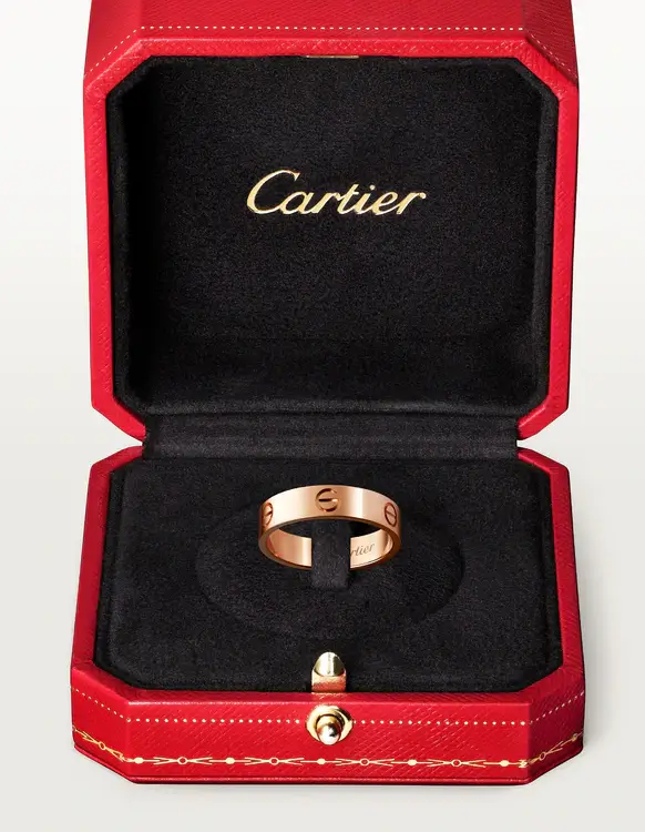 Kırmızı, kapak iç kısmında altın rengi Cartier logosu bulunan lüks kutusunun siyah kadife zemininde özenle sergilenen, üzerinde karakteristik vida motifleri ve ince bir harf detayı barındıran göz alıcı bir rose gold Cartier Love yüzük.
