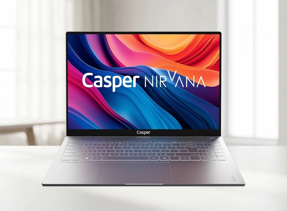 Gümüş renkli, modern tasarımlı Casper Nirvana S100 dizüstü bilgisayar, parlak beyaz bir masa üzerinde önden çekilmiş bir açıyla dururken, canlı renkli soyut bir duvar kağıdı ve Casper NIRVANA logosunu gösteren 16 inçlik ekranı, alüminyum kasasının şıklığını ve aydınlatmalı klavyesini vurguluyor.