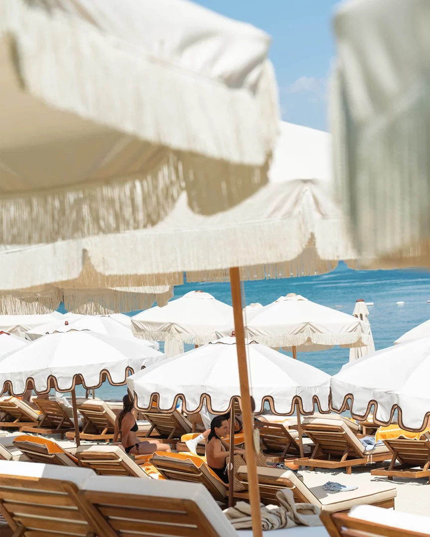 Bodrum Demirbükü'ndeki Lucca Beach'in yeni dönemini yansıtan bu çekimde, masmavi denize karşı şık beyaz saçaklı şemsiyeler ve rahat şezlonglarda dinlenen misafirler, markanın deneyim odaklı Akdeniz yaşam kültürü anlayışını gözler önüne seriyor.