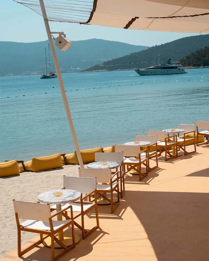 Bodrum Demirbükü'ndeki Lucca Beach'in yeni döneminde, masmavi denize nazır uzanan sade ve şık Akdeniz estetiğindeki bembeyaz masa ve sandalyelerin, sarı minderlerin çevrelediği kumlu kıyı, yemyeşil tepeler ve lüks yatlarla sakin bir yaşam kültürünü deneyim sunuyor.
