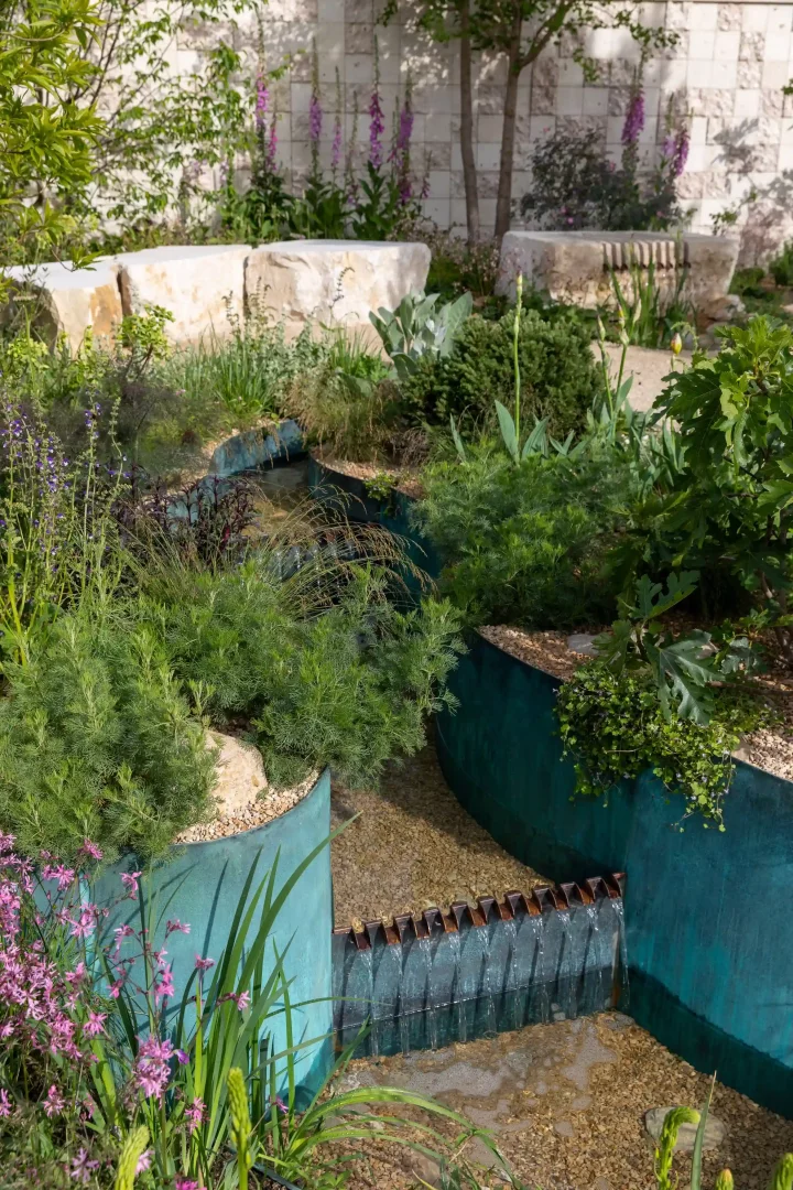 Bakır patinalı metal kanallardan şık basamaklarla akıp giden suyun öne çıktığı bu modern ve doğal bahçe tasarımı, Chelsea Flower Show 2026’da sergilenen bahçe trendleri arasında yer alan suyun geri dönüşü ve sakin, yaşanabilir alanlar temasını vurguluyor.