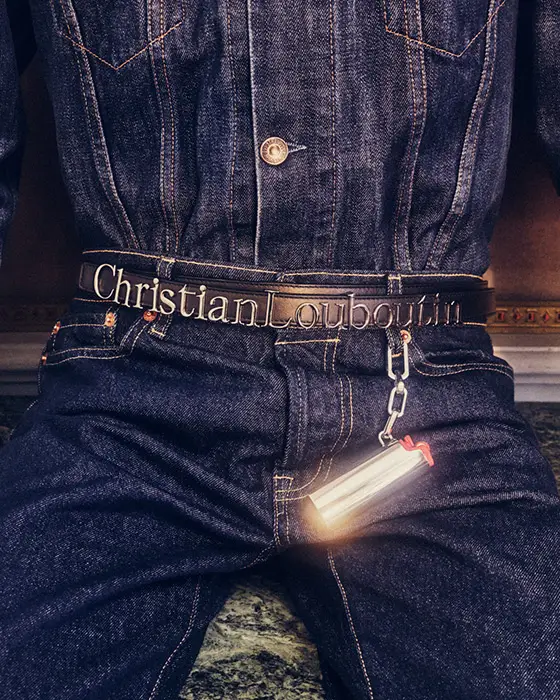 Christian Louboutin'in sonbahar-kış koleksiyonundan bir stil örneği sunan bu yakın planda, koyu renk jean ceket ve pantolon giyen bir kişinin belinde marka isimli siyah deri kemer ile jean pantolonun kemer halkasına takılı, parlayan metalik bir aksesuar dikkat çekiyor.