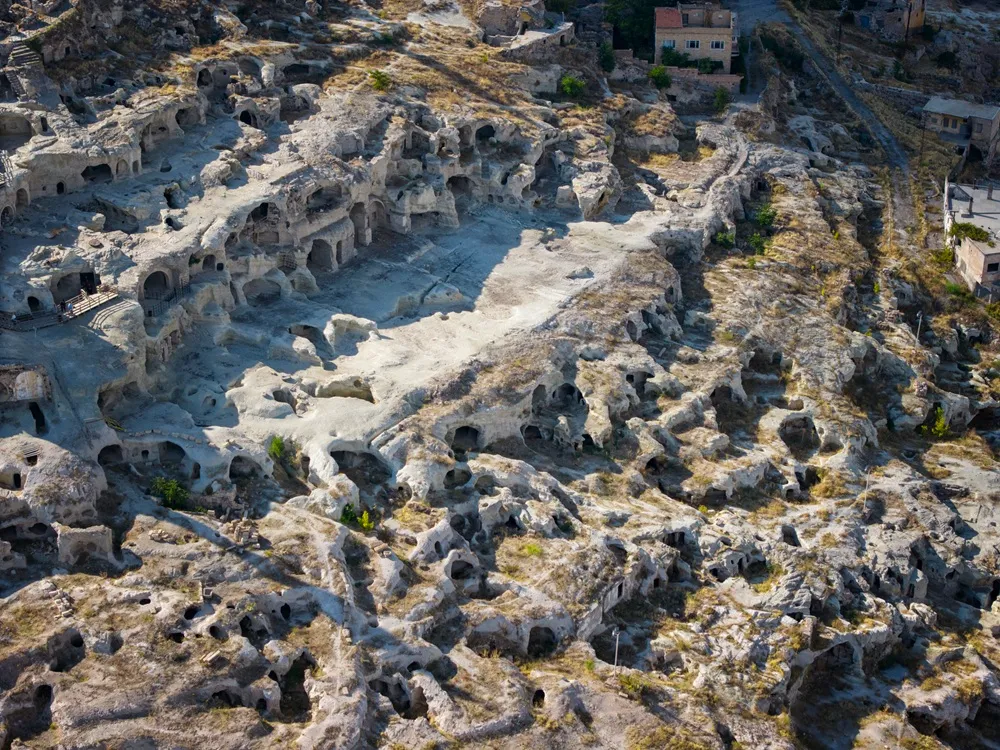 Kapadokya'nın kendine özgü coğrafyasını sergileyen bu kuşbakışı fotoğrafta, kuru otlarla kaplı açık renkli kayalıklara oyulmuş çok sayıda mağara ev ve antik yerleşim yeri dikkat çekiyor, Derinkuyu bölgesinin tarihi dokusunu gözler önüne seriyor.