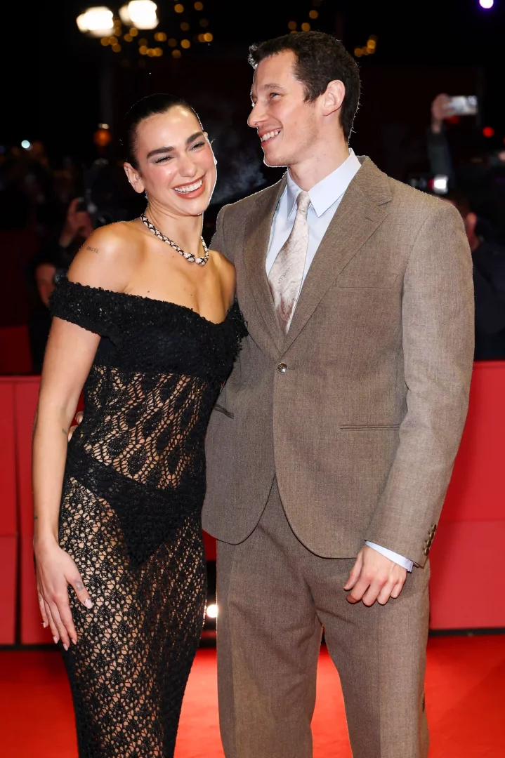 Kırmızı halıda neşeli bir şekilde birbirlerine bakarak gülümseyen Dua Lipa, omuzları açık siyah file detaylı elbisesi ve kolyesiyle göz kamaştırırken, yanındaki Callum Turner açık kahverengi takım elbisesi ve kravatıyla uyumlu bir görünüm sergileyerek postun konusu olan celebrity çiftin ilgi odağı olduğunu vurguluyor.