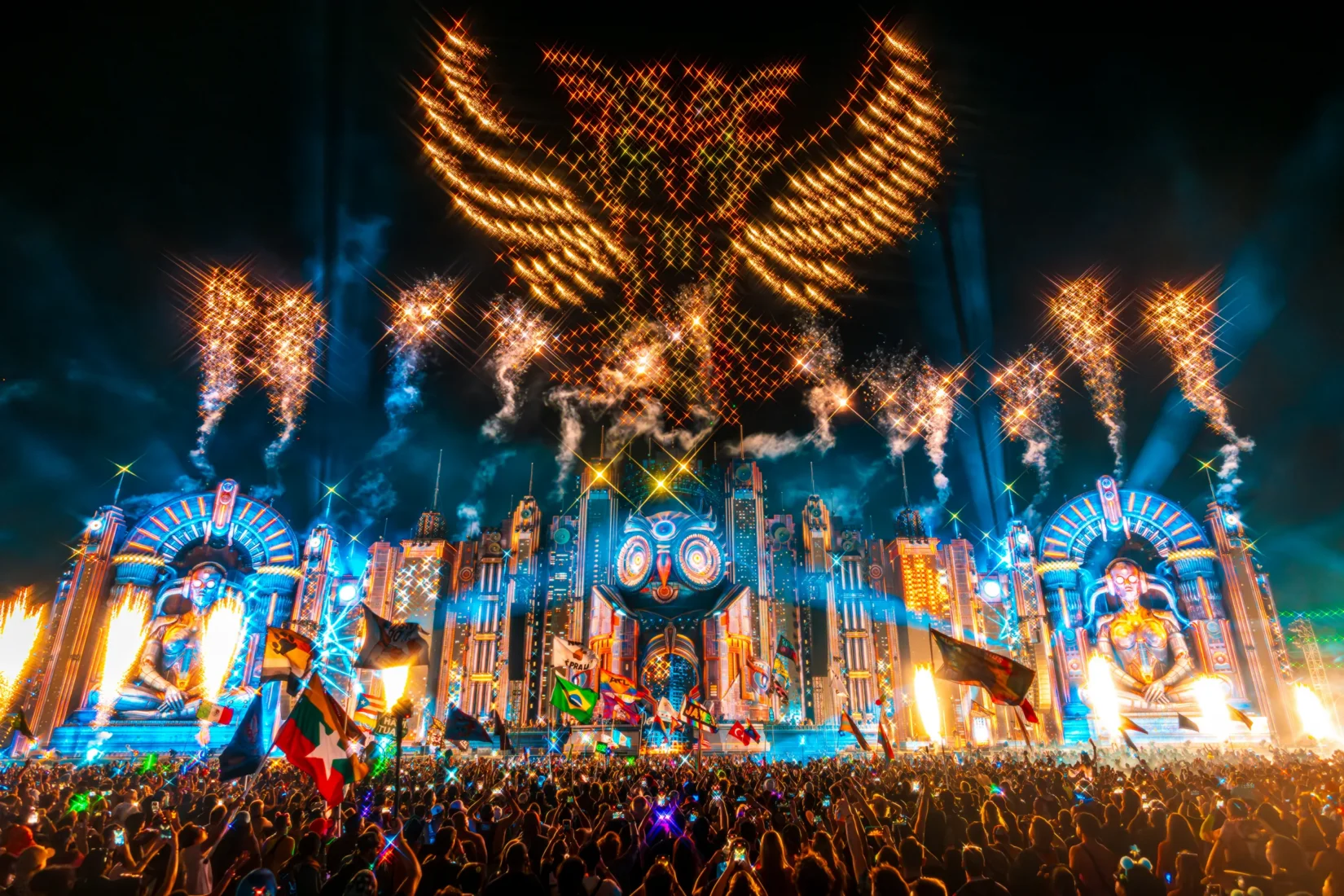 Gece vakti, binlerce kişinin coşkuyla bir araya geldiği Electric Daisy Carnival'ın devasa, LED ekranlarla donatılmış, ışıl ışıl parlayan sahnesinin önündeki kalabalığı gösteren geniş açılı bir fotoğraf.