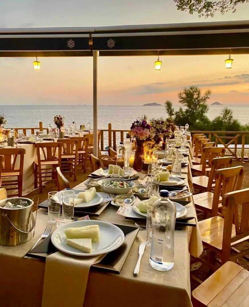 Gün batımında denize nazır bir terasta, beyaz peynir ve çeşitli mezelerle donatılmış uzun bir masa, pekmez önerileri gibi lezzetlerin de düşünülebileceği, mum ışığında keyifli bir ziyafet ortamı sunuyor.