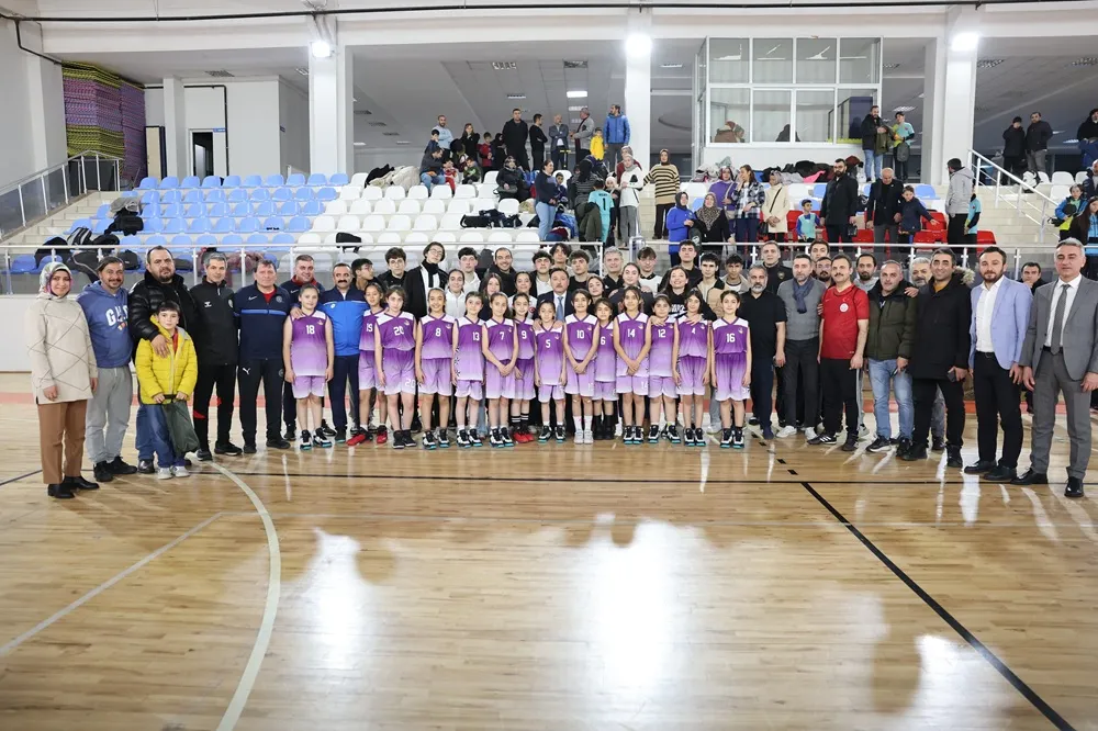 Kapalı bir spor salonunun parlak ahşap zeminli kortunda, mor-beyaz formalar giyen genç kız sporculardan oluşan Erva'nın da aralarında bulunduğu bir takımın, antrenörler, yöneticiler ve ailelerle birlikte tribünlerin önünde objektife gülümsediği büyük bir grup fotoğrafı.