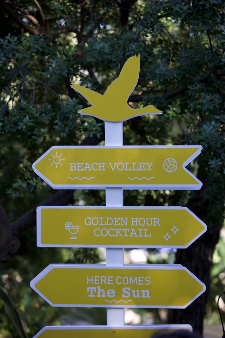 Sarı ve beyaz renklerdeki bir direğin üzerinde, uçan bir kuş silüetiyle birlikte Beach Volley, Golden Hour Cocktail ve Here Comes The Sun gibi yazılar taşıyan yön tabelaları, Bodrum'un eğlence dolu 'golden summer' atmosferini yansıtan keyifli seçenekleri işaret ediyor.