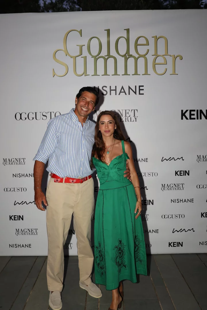 Bodrum'daki Golden Summer etkinliğinde, beyaz ve mavi çizgili gömlekli bir beyefendi ile yeşil işlemeli elbiseli, zarif takılar takmış bir hanımefendi, arkalarında büyük altın harflerle Golden Summer ve Nishane logolarının yer aldığı şık bir fon önünde gülümseyerek poz veriyor.