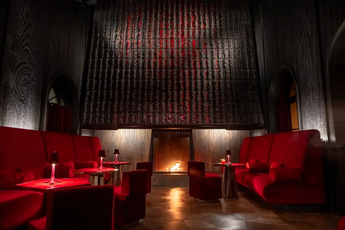 Koyu ahşap panelli duvarlar ve şömine ateşiyle sıcak bir şekilde aydınlatılan Banks Bar Lounge'da, lüks kırmızı kadife koltuklar ve ışık yansıtan modern masalar loş, samimi bir atmosfer sunuyor.