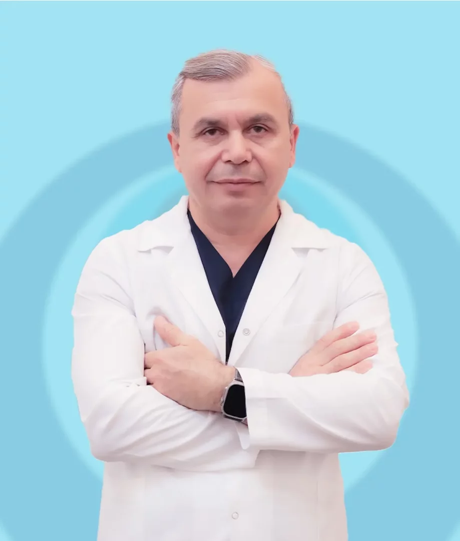 Halil Genç, lacivert cerrahi forma üzerine beyaz önlük giymiş, kollarını göğsünde kavuşturmuş ve ciddi bir ifadeyle doğrudan kameraya bakarken, arkasında açık mavi tonlarda dairesel desenli bir arka plan yer alıyor.