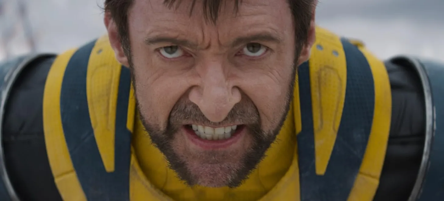 Hugh Jackman, Deadpool & Wolverine filminden ikonik sarı ve mavi kostümü içinde, karakterin sinema kariyerine damga vuran öfkesini ve kararlılığını yansıtan kükreyen, dişlerini sıkmış bir ifadeyle kamera önünde duruyor.