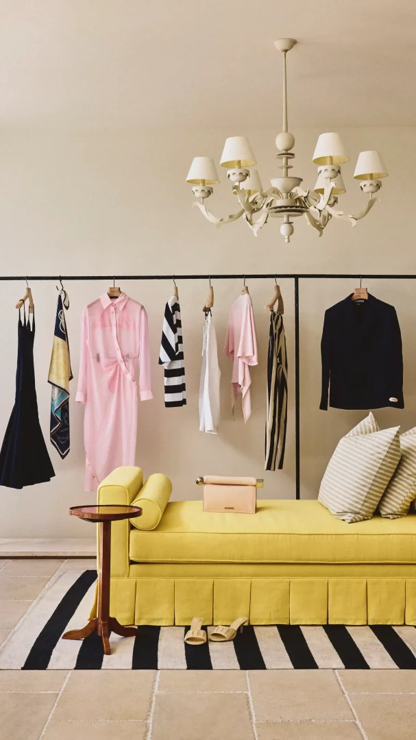 Bodrum'daki Jacquemus moda pop-up mağazasının Akdeniz estetiğini yansıtan bu şık köşede, sarı renkli bir sedir, siyah beyaz çizgili halı, pastel tonlarda elbiseler ve aksesuarların sergilendiği bir askılık ile zarif bir avize dikkat çekiyor.