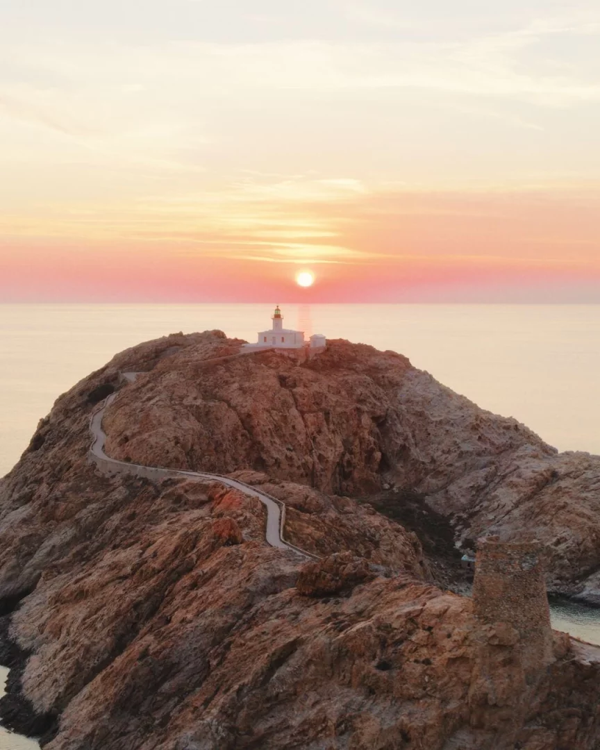 Korsika'nın Phare de la Pietra deniz fenerinin bulunduğu kayalık yarımada üzerinde, gün batımının turuncu ve pembe tonlarıyla aydınlanan, etrafında Akdeniz'in sakin sularının uzandığı bu etkileyici manzara, Jacquemus defilesine doğal bir fon oluşturuyor.