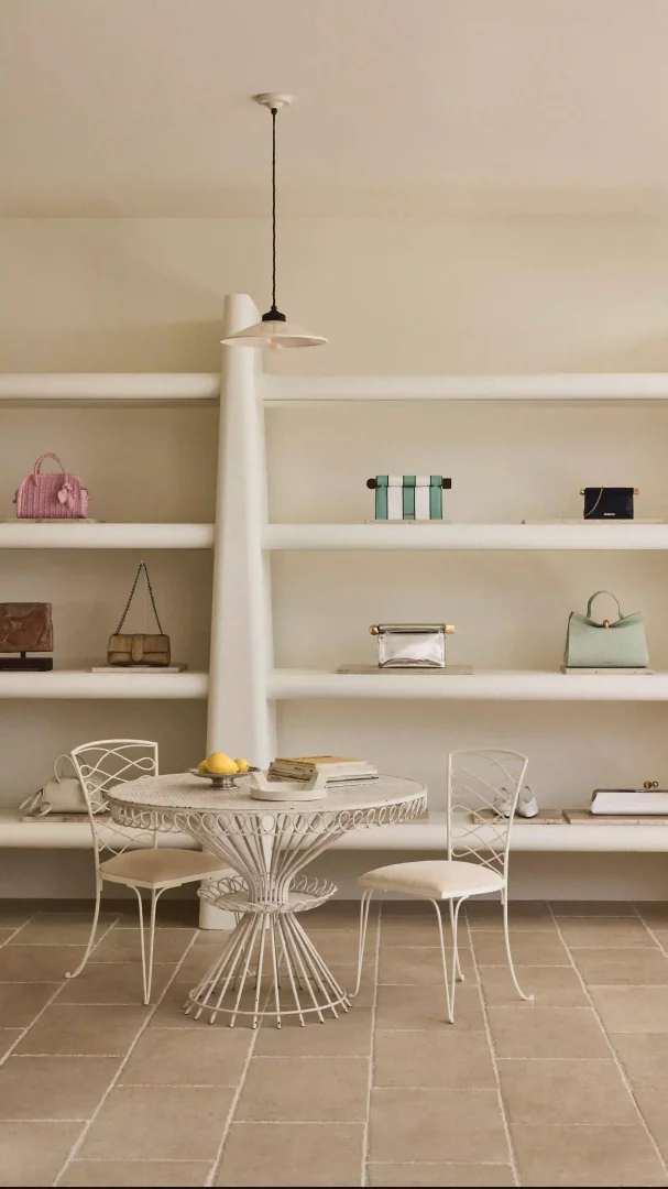 Açık renk fayans zeminli ve beyaz dalgalı raflı bir Jacquemus butiğinde, pembe, yeşil, siyah, altın ve gümüş tonlarında lüks çantalar sergilenirken, Mandarin Oriental Bodrum'un Akdeniz estetiğine uygun beyaz ferforje masa ve sandalyeler ile limonlar göz alıyor.