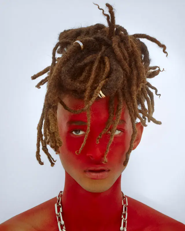 Jaden Smith'in yüzü ve boynu parlak kırmızı boya ile kaplanmış, yüzüne düşen kahverengi rasta saçları ve kalın gümüş zincir kolyesiyle dikkat çeken, Christian Louboutin işbirliği ruhunu yansıtan çarpıcı ve sanatsal bir portre.