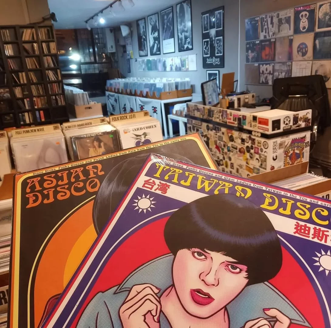 Ön planda renkli Taiwan Disco ve Asian Disco plak kapaklarının öne çıktığı, arka planda ise Post Punk New Wave, Folk Rock gibi çeşitli türlerdeki yüzlerce plağın rafları ve kutuları doldurduğu, canlı bir plak dükkanı iç görünümü.