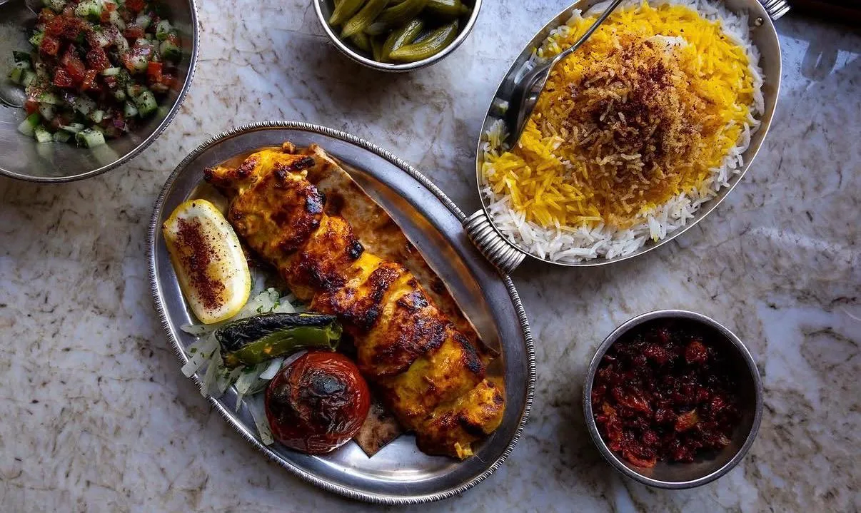 Mermer görünümlü bir masanın üzerinde, mangalda pişirilmiş, nar gibi kızarmış tavuk kebabı, safranlı pirinç pilavı, ızgara domates, biber ve limon dilimi, ince doğranmış soğanlı yeşillikler, çoban salata, turşu ve özel bir sosla dolu tabaklar, Londra'daki zengin mutfak kültürünü yansıtan iştah açıcı bir ziyafeti gözler önüne seriyor.