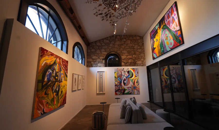 Alaçatı'nın modern ve geleneksel mimarisini birleştiren geniş bir iç mekanda, renkli çağdaş sanat eserlerinin sergilendiği beyaz duvarlar ve kemerli pencereler ön plana çıkarken, zarif desenli dekoratif tavan ve konforlu uzun bir koltuk alanı davetkar bir atmosfer sunuyor.
