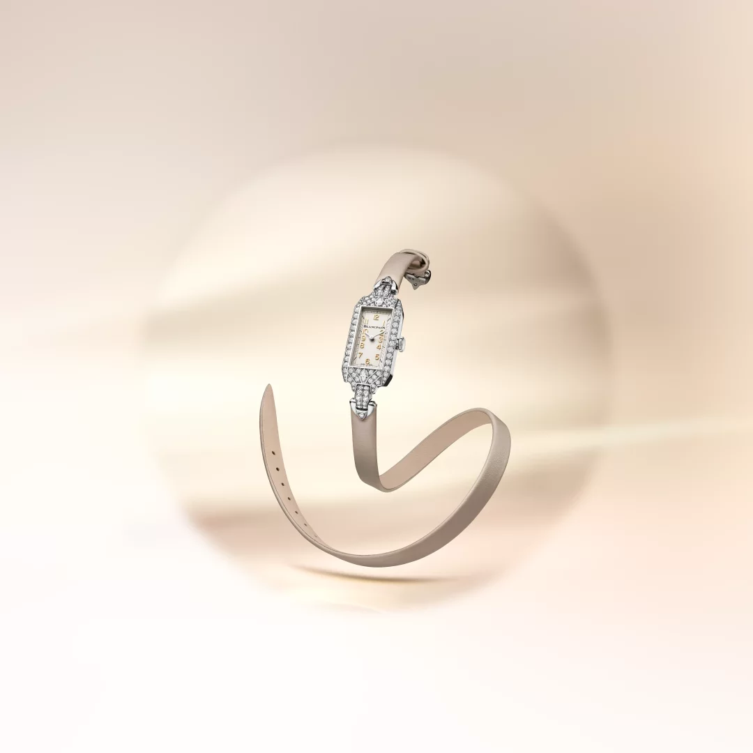 Açık bej renkli deri kayışı zarifçe kıvrılmış, pırlantalarla süslenmiş beyaz altın dikdörtgen kasaya sahip, Art Deco etkili kadranında altın indeksler ve Blancpain logosu görülen bu lüks Marilyn Monroe Ladybird Tribute koleksiyon saati, açık renk bir zeminde adeta süzülerek göz kamaştırıyor.