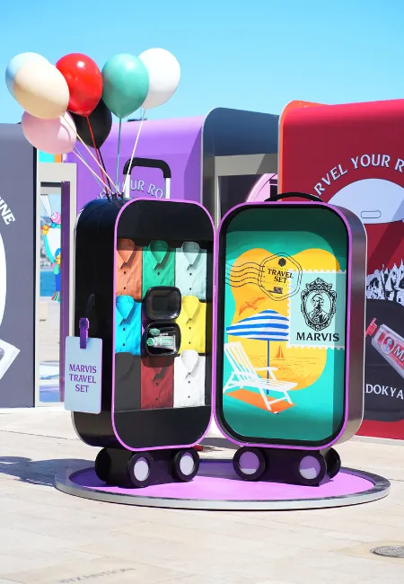 Marvis Travel Set etiketiyle, birinde rengarenk gömlekler ve küçük boy kişisel bakım ürünleri, diğerinde ise şezlong ve şemsiyeli canlı bir plaj çizimi görünen, üstünden renkli balonlar yükselen iki mor tekerlekli açık bavul, markanın Haziran ayındaki yeni tasarımlarını ve gelişmelerini vurguluyor.