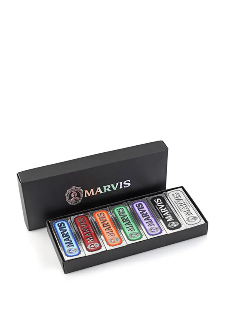 Beyaz bir zeminde duran, kapağı açık siyah Marvis kutusunun içinde, mavi, kırmızı, turuncu, yeşil, mor ve gümüş renginde, her birinin üzerinde Marvis logosu bulunan altı adet seyahat boyu diş macunu tüpü şıkça dizili.