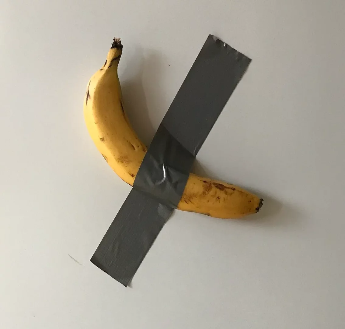 Maurizio Cattelan'ın Comedian adlı çağdaş sanat eserine gönderme yapan bu görselde, sarı renkli, hafif kahverengi lekelerle olgunlaşmış bir muz, gri renkteki iki parça güçlü koli bandı ile açık renkli düz bir duvara çaprazlamasına sağlamca yapıştırılmış durumda.