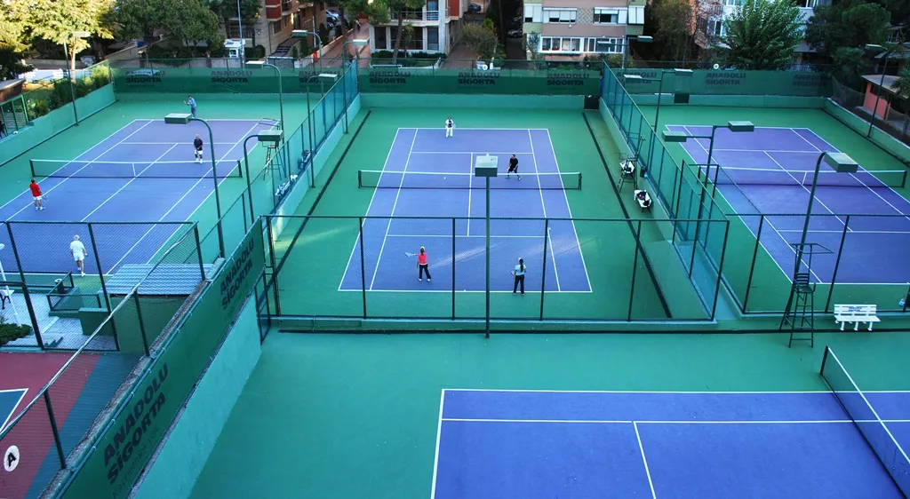 Miltas Spor Tesisleri bünyesindeki yeşil zeminli ve mavi çizgili birden fazla tenis kortu kuşbakışı görünümde; bazı kortlarda oyuncular tenis oynarken, çevredeki Anadolusigorta reklamlı çitler ve aydınlatma direkleri dikkat çekiyor.
