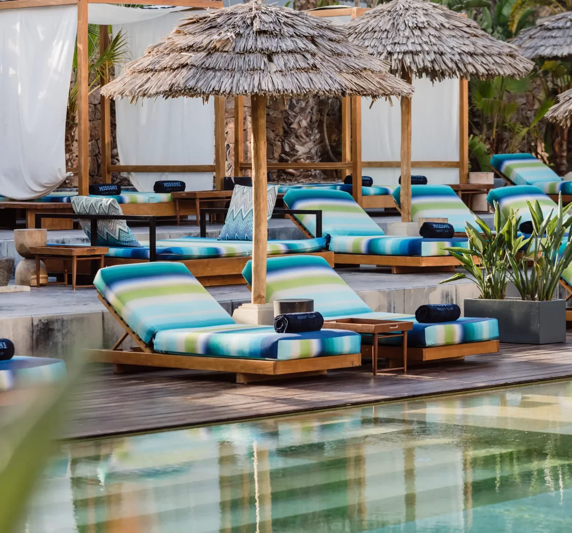 Missoni Resort Club ve OKU Ibiza iş birliğini yansıtan, Missoni'nin ikonik desenlerinden esinlenmiş mavi, turkuaz ve yeşil çizgili minderlerle donatılmış ahşap şezlongların, hasır şemsiyelerin ve beyaz perdeli kabinlerin sıralandığı, yazın en gözde beach club'ları arasında yer alan moda evlerinin sunduğu lüks bir havuz başı tatil deneyimi.