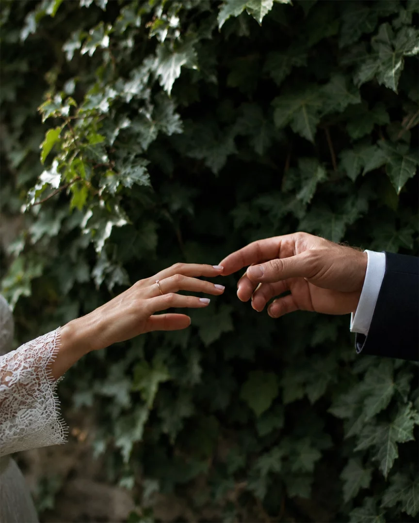 Yeşil sarmaşıklarla bezeli bir duvarın önünde, dantel kollu gelinlik giyen ve yüzük takılı bir kadının eli ile takım elbiseli bir erkeğin eli, romantik bir fotoğraf pozu verirken nazikçe birbirine uzanıyor.