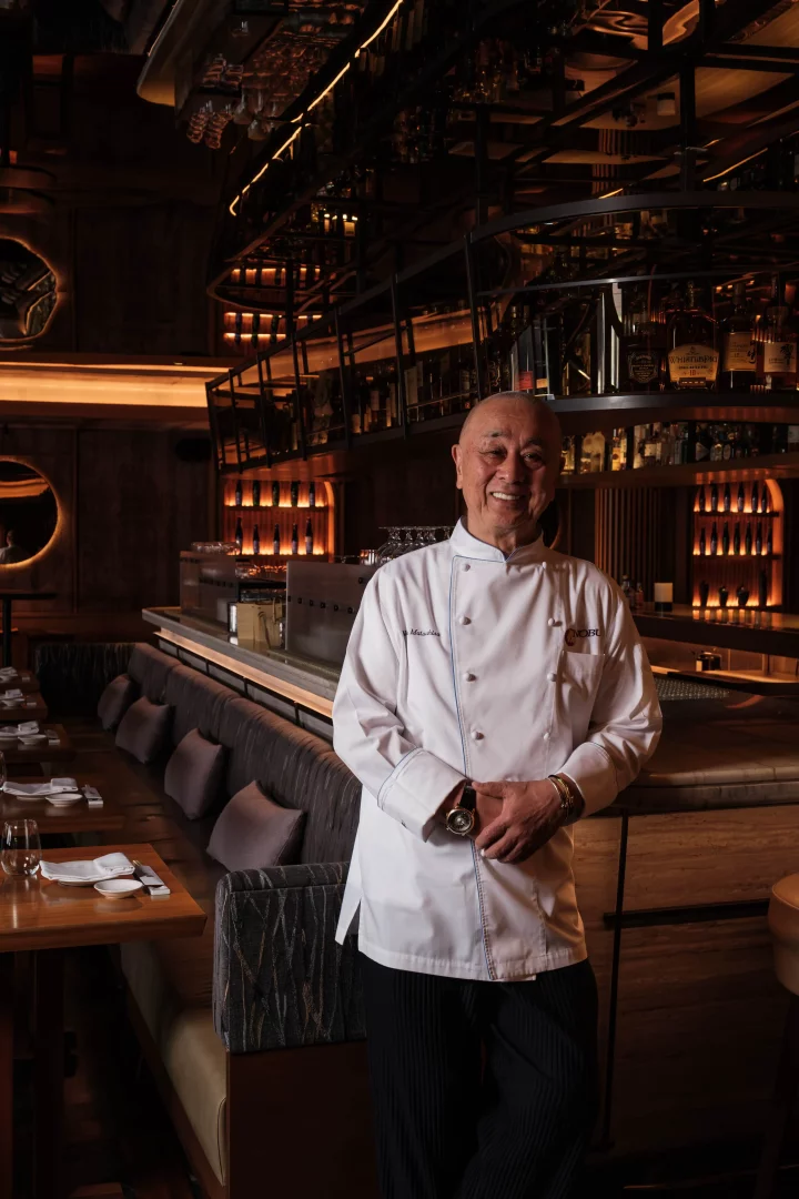 Nobu İstanbul'un zarif ve sıcak bir atmosfer sunan, arkasında şık bir bar ile modern detaylarla döşenmiş restoranında poz veren dünyaca ünlü Şef Nobu Matsuhisa, markanın beşinci yılına özel menüsü ve mutfak felsefesini yansıtan bir gülümsemeyle objektife bakıyor.