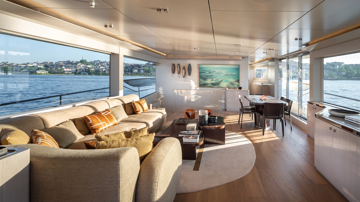 Büyük camlarından deniz ve karşı kıyı şehir manzarası görünen, Numarine 27XP Explorer yatın geniş ve aydınlık salonu, modern sanat eserleri ve rahat bir oturma grubu ile açık renk ahşap zemini birleştirerek lüks ve ferah bir atmosfer sunuyor.