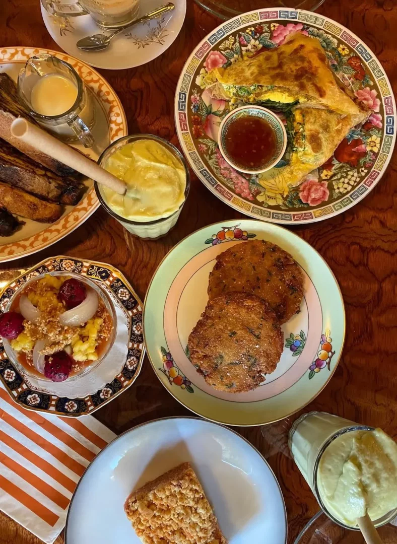New York'taki Dua restoranında üstten çekilen bu karede, ortada soslu üçgen dolgulu gözleme, sağda iki kızarmış mücver, solda meyve ve granola kasesi, üstte kremalı bir sürahi ve kızarmış muz dilimleri ile sarı içeceklerin yer aldığı zengin bir masa gözüküyor.