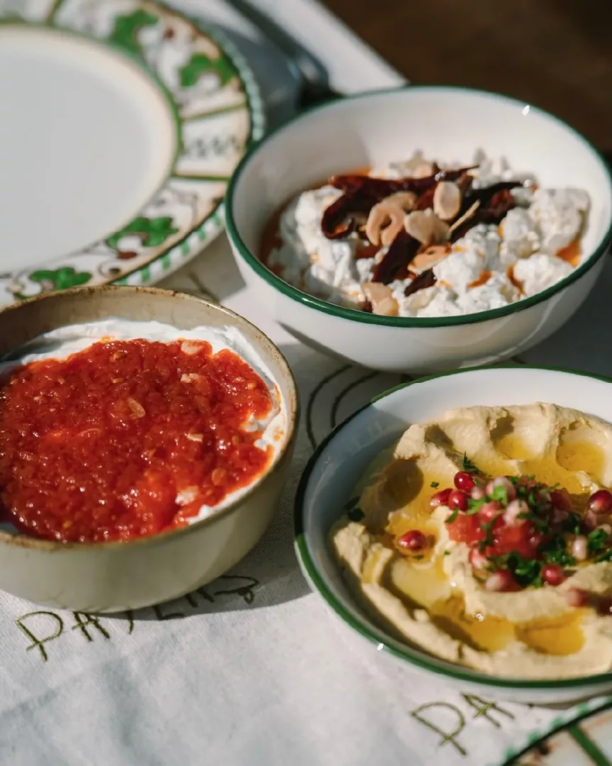 Beyaz masa örtüsü üzerinde, zeytinyağlı humus üzerine nar taneleri, kırmızı biberli yoğurtlu meze ve kurutulmuş biber ile bademle zenginleştirilmiş süzme yoğurt gibi Pay Alaçatı'nın geleneksel ve modern lezzetlerini bir araya getiren üç ayrı meze kasesi.