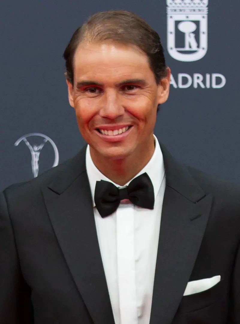 Ünlü tenisçi Rafael Nadal, koyu renk smokini, beyaz gömleği ve siyah papyonuyla kameraya içtenlikle gülümserken görülüyor; arka planda ise flu bir şekilde logo ve Madrid yazıları seçilen resmi bir etkinlik atmosferi dikkat çekiyor.