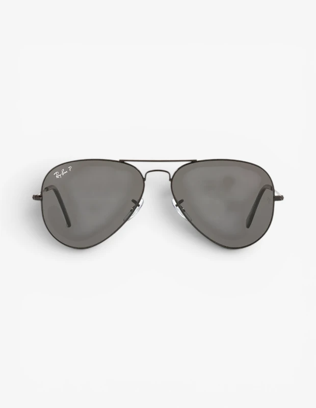 Beyaz, sade bir arka plan üzerinde konumlandırılmış, ikonik tasarıma sahip, parlak siyah metal çerçeveli ve sol camında belirgin Ray-Ban P logosu bulunan koyu füme renkli polarize camlı Ray-Ban Aviator güneş gözlüğü, hem stil sahibi hem de göz koruması için mükemmel bir seçenek sunuyor.
