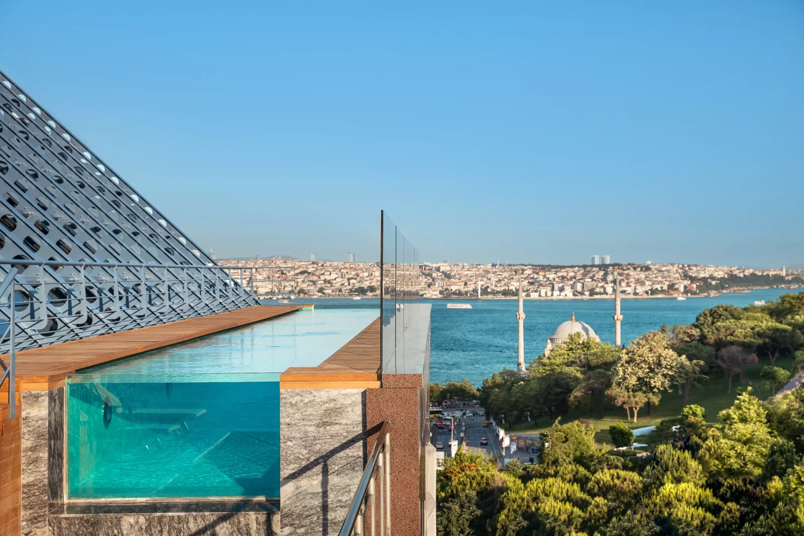 Ritz-Carlton Istanbul'un modern mimariye sahip terasındaki cam kenarlı sonsuzluk havuzunda yüzen bir kişinin görüldüğü panoramik manzara; masmavi Boğaz'ın, tarihi caminin ve karşı kıyıdaki İstanbul silüetinin büyüleyici birleşimini sergiliyor.