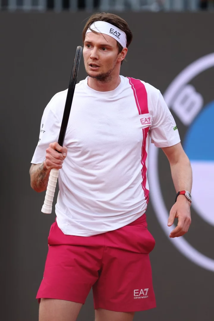 Tenis kortunda, beyaz kafa bandı ve pembe detaylı beyaz tişörtüyle raketini tutan Alexander Bublik'in sağ bileğinde, Roland Garros turnuvasına uygun sportif duruşuyla belirgin Bianchet Tourbillon B1.618 Open Work bağımsız fıçı kasa kol saati görülüyor.