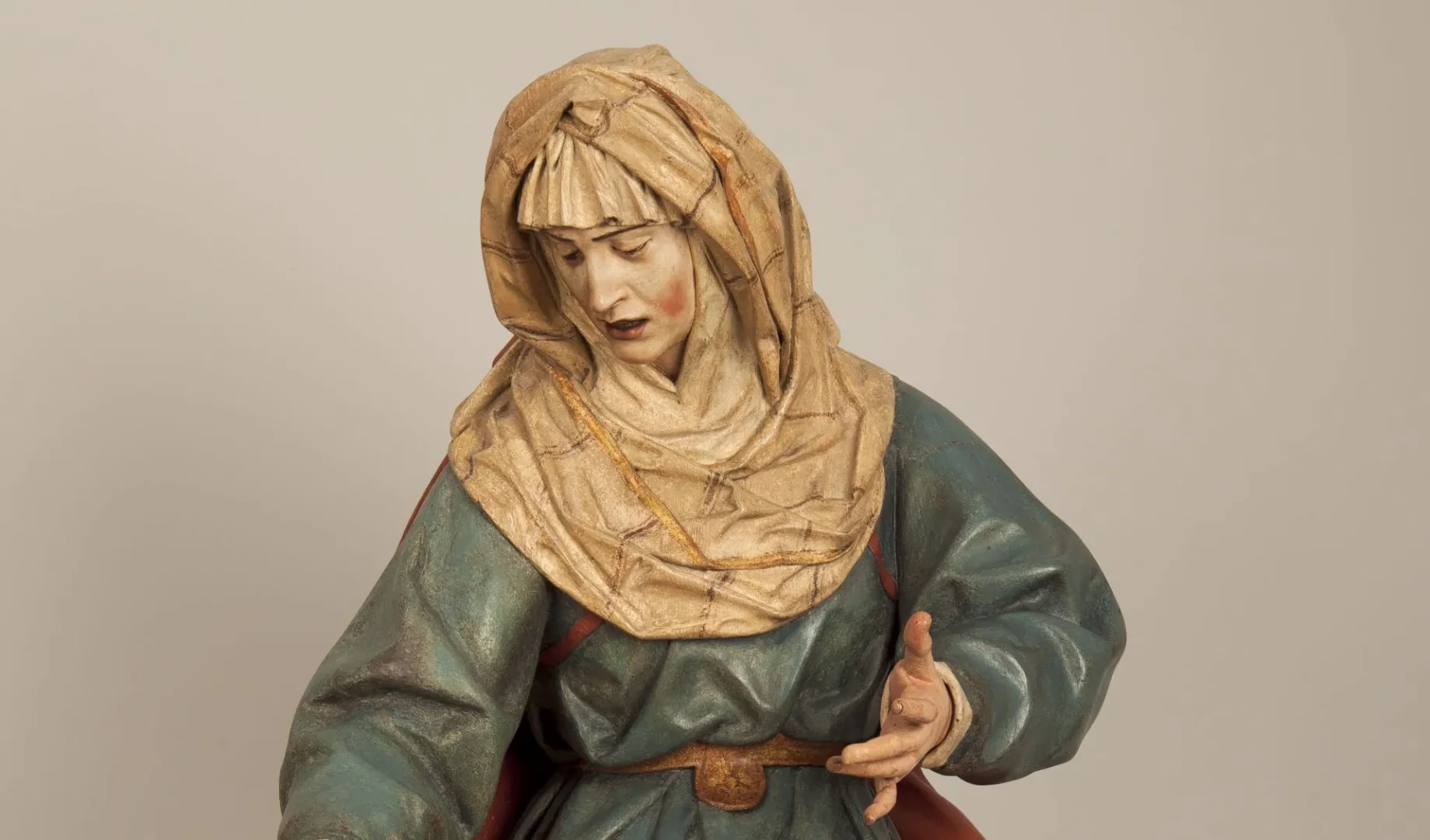 Soluk pembe yanaklı, başı hafifçe öne eğik, hüzünlü yüz ifadesiyle Veronique'i tasvir eden bu ahşap heykel, zamanın yıpratıcı etkilerine rağmen canlı kalan boyama renkleriyle dikkat çekiyor; fırfırlı krem rengi başörtüsü ve turkuaz tuniğiyle, nazikçe uzanan sağ eliyle duygusal bir duruş sergiliyor, heykeltıraşlık detaylarını gözler önüne seriyor.